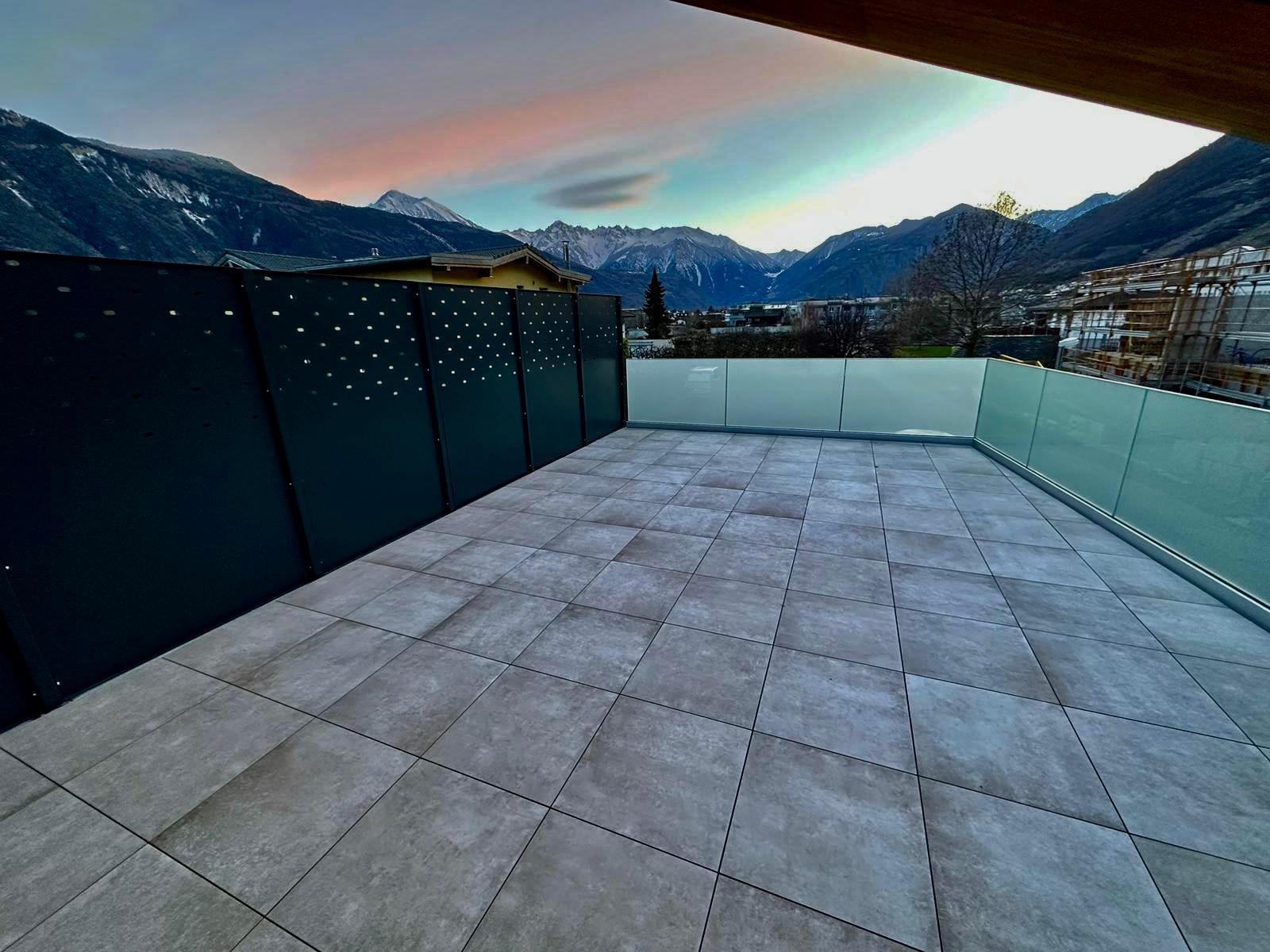 Terrasse au coucher du soleil : brise-vue perforé et garde-corps vitré — Verdan, Fully (VS)